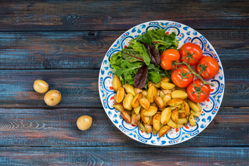 Fried baby potatoes, green salad and fresh tomatoes on a big plate in rustic style