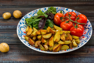 Fried baby potatoes, green salad and fresh tomatoes on a big plate in rustic style