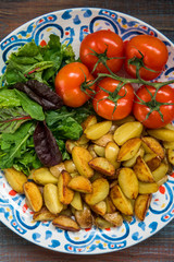 Fried baby potatoes, green salad and fresh tomatoes on a big plate in rustic style