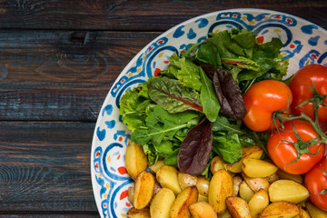 Fried baby potatoes, green salad and fresh tomatoes on a big plate in rustic style