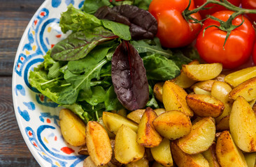 Fried baby potatoes, green salad and fresh tomatoes on a big plate in rustic style