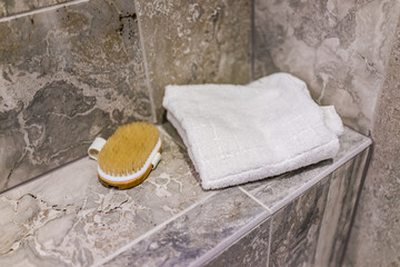 Closeup of staging shower towel and brush in modern stone grey bathroom seat bench in model home, apartment or house