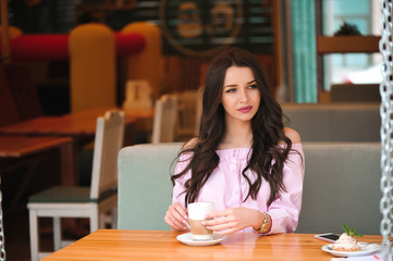 Woman drinking hot cappuccino coffee and eating cake at cafe.