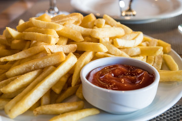 French fries in a white plate and ketchup on a table