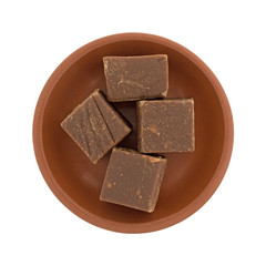 Top view of four chunks of butter chocolate fudge in a small red clay bowl isolated on a white background.