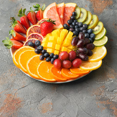 Assortment of cut fruits in rainbow colours oranges grapes mango strawberries kiwis blueberries grapefruit on the grey concrete table, copy space, selective focus