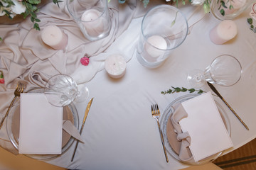 On the table, decorated for the wedding ceremony in restaurant, a many candles, white dishes, glasses, bouquets with fresh flowers and modern wedding decor stand on a light tablecloth. Top view