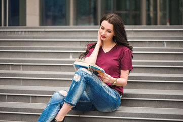 Beautiful woman reading a book on the steps of the building.