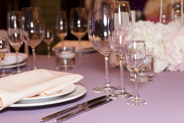 A stylish wedding decor of dishes, white bouquets with flowers, candles and glasses stand on a light tablecloth of a served table. Side view, selective focus
