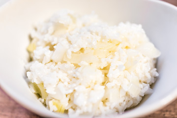 Macro closeup of cooked sticky sweet glutinous medium grain rice in white bowl with fresh yellow onions on table, detail, texture