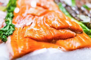 Seafood stand with cuts and filets of orange farmed salmon on ice with kale leaves