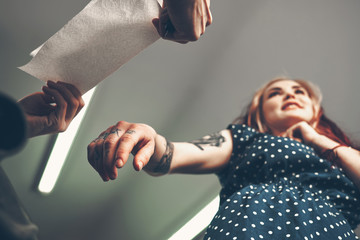 Young beautiful girl looks like the tattoo artist does the tattoo, reading the news in the...