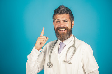 Medicine, clinic, treatment and healthcare concept - friendly bearded medical doctor with stethoscope in white coat raised finger up. Advertising hospital, clinic, pharmacy. Copy space in upper corner