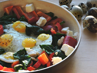 Appetizing fried quail eggs with spinach, feta cheese and peppers.