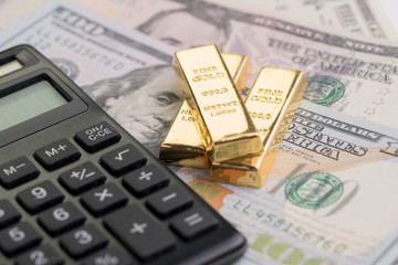 Gold bars or bullion ingot on pile of money US dollar bills with calculator, success investment or...