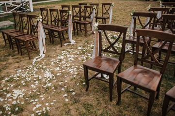 Fototapeta na wymiar Very beautiful outside ceremony. classical wedding in forest. The arch is wooden. White flowers. Brown chairs. Rite. Bride and groom. Decor. Floristics. In the open air. Path from the petals of roses.