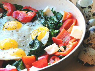 Appetizing fried quail eggs with spinach, feta cheese and peppers.