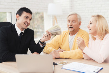 Mature couple at a reception with a lawyer. The lawyer holds a bundle of money and smiles.