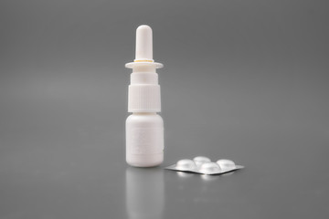 medical thermometer with tablets and a spray for the nose on a gray background in the studio.