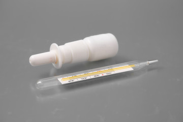 medical thermometer with tablets and a spray for the nose on a gray background in the studio.