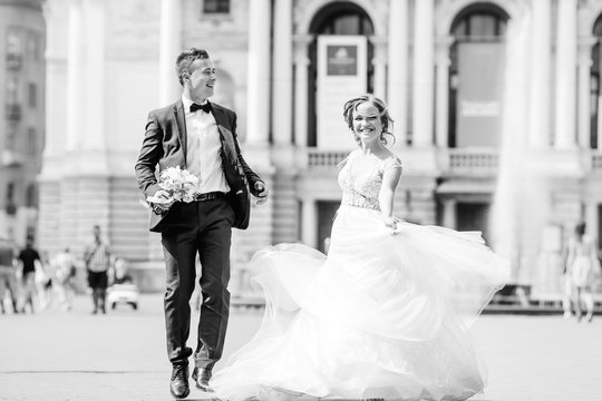Newlyweds laughing and dancing on the square near a beautiful building on black and white photography