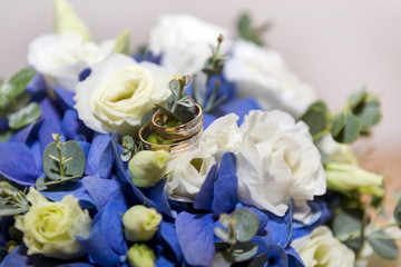 gold wedding rings on a bouquet of white and blue flowers
