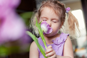 Portrait of beautiful little girl with bouquet of purple flowers.