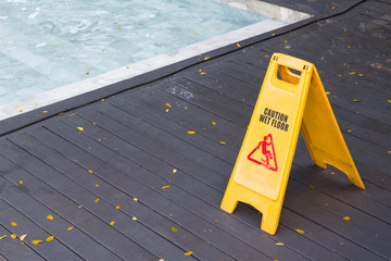 warning yellow plastic sign beside swimming pool, caution wet floor on wooden floor