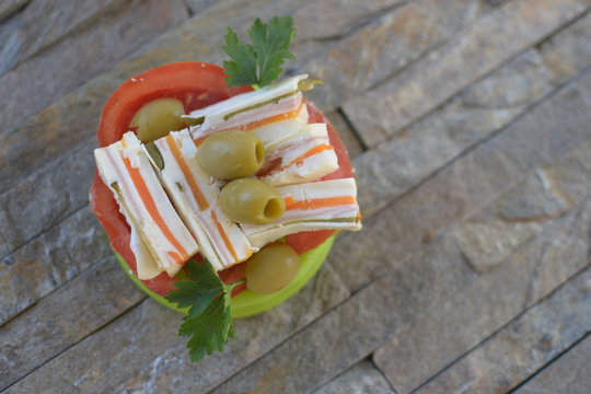 orange white salty cakes on tomato rings with olives near and from above parsley on green plate on rectangular swen stone