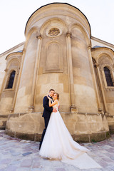 beautiful newlyweds hugging and looking at camera lens against the background of the building