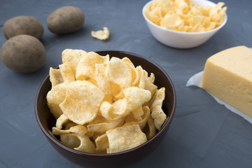 Potato chips with cheese in a plate that is located on a gray background.