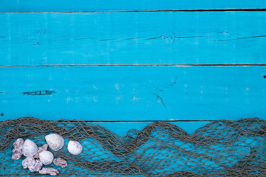 Blank rustic teal blue wood sign with seashells and fish netting border; wooden background with painted copy space