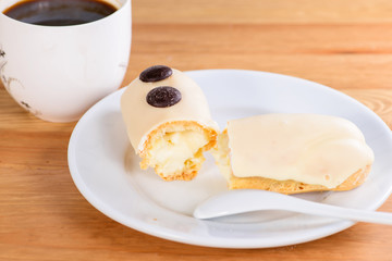 Appetizing sweet dessert. White glaze cupcake with cream and cup of coffee on the wooden table