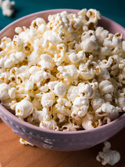 Popcorn in pink bowl on wooden board on dark green background