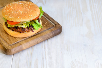 Delicious tasty burger with beef, tomatoes, salad and sauce on light wooden board on brown background