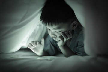 Boy watching online screen tablet, under duvet. © vinnstock