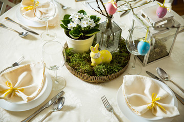 Beautiful served round table with decorations in dining room. Little yellow bunny, willow branches decorated with colorful Easter eggs. Spring holiday setting. Top view shot