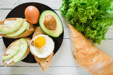 Sandwiches with avocado and egg on black plate on wooden table. Delicious natural breakfast