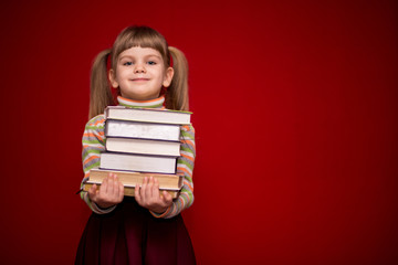 Portrait of cheerful little girl isolated on red hold many books. Concept of knowledge or school. Book lover.