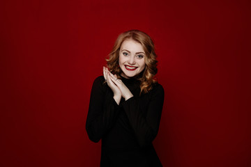 young cheerful red-haired girl in black clothes posing in the studio isolated on red background. body language and emotions. woman smiling into camera rejoicing her success. 
