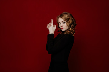 young cheerful red-haired girl in black clothes posing in the studio isolated on red background....