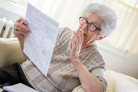 Shocked senior woman looking at bills.