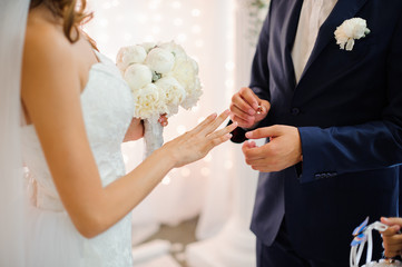 groom puts on a gold wedding ring on the finger of a beautiful bride