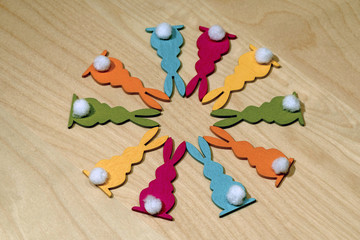 Ten colorful wooden Easter bunnies with a little white tail in a circle on a wooden underground