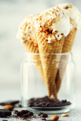 Caramel sauce ice cream in waffle cone with coffee beans on grey stone background. Summer food concept, copy space. Healthy gluten free ice-cream. Banner
