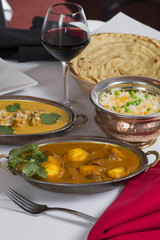 Indian curry food spread on a fancy dinner table with rice, laccha paratha, lamb aam wala, saffron malai kofta, red wine
