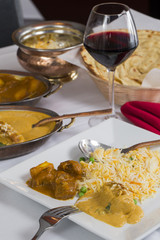 Indian curry food spread on a fancy dinner table with rice, laccha paratha, lamb aam wala, saffron malai kofta, red wine