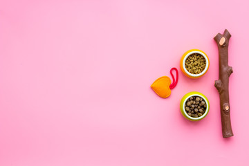 Pet care concept. Toys near bowls with animal feed on pink background top view copy space