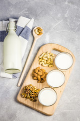 Almonds, cashew, walnuts and nut milk in glasses on wooden board on concrete background. Top view, space for text.