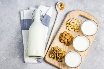 Nut mix and nut milk in glasses on wooden board on concrete background.Top view, space for text.
